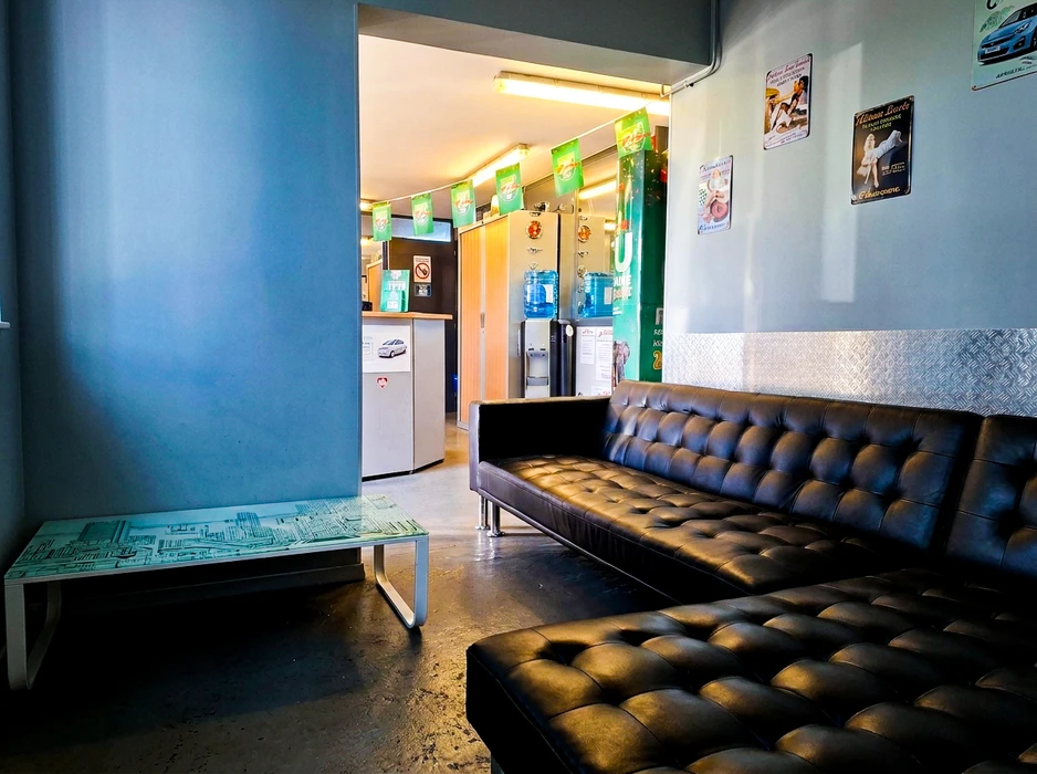 Salle d'attente d'un garage automobile avec canapé en cuir noir capitonné, table basse en verre sérigraphié