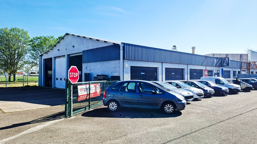 Garage automobile avec parking extérieur, bâtiment industriel bleu et gris avec plusieurs portes de levage