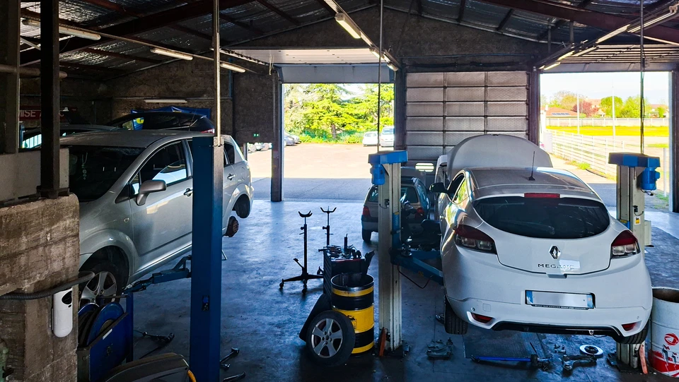 Mécanicien automobile en combinaison travaillant sous le capot ouvert d'un véhicule dans un garage professionnel