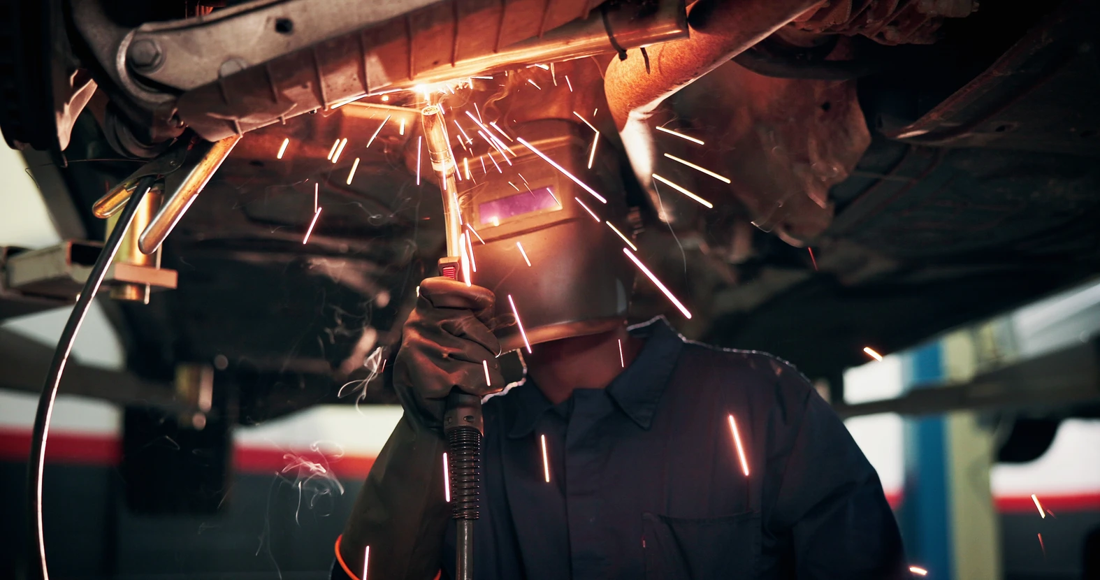 Mécanicien automobile travaillant sous un véhicule surélevé dans un garage professionnel